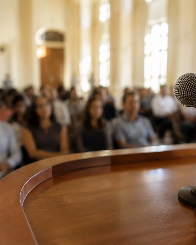 Microfone montado sobre a tribuna, com o público sentado fora de foco atrás